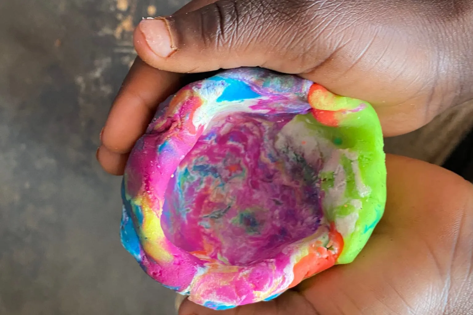 A child's cupped hands hold a bowl shaped from brightly coloured play dough, at a play therapy session for young children in Zimbabwe